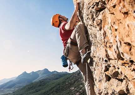 Mann beim Klettern aus niedriger Perspektive vor dem Himmel